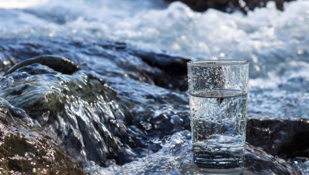 Glass of water with flowing stream in background