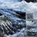 Glass of water with flowing stream in background