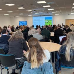 A group of people sat around tables at Arable Futures watching a presentation